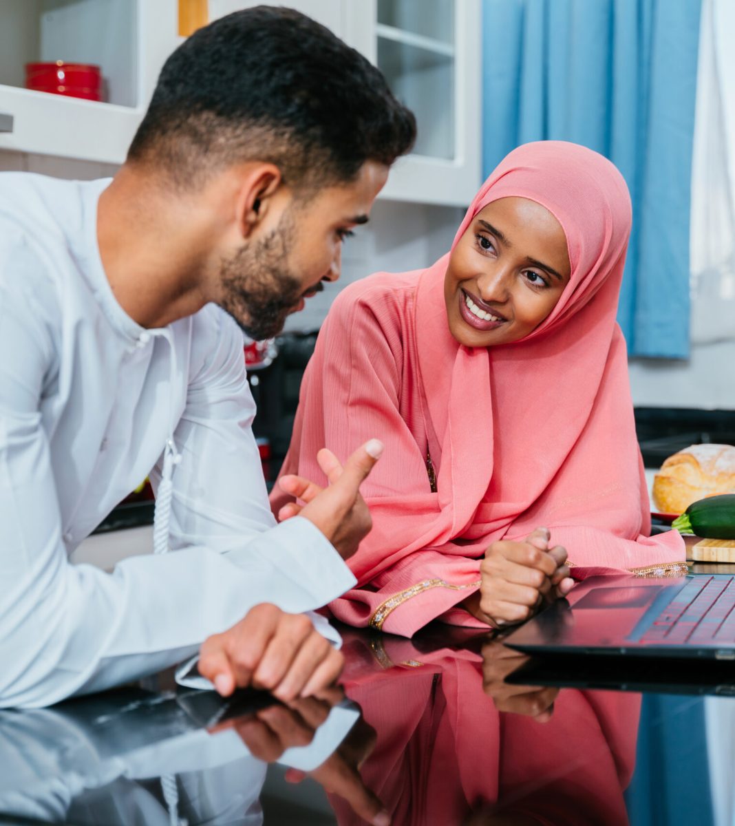 Happy middle-eastern couple wearing traditional arab clothing at home - Married arabian husband and wife bonding together in the apartment, concepts about relationship, domestic life and emirati lifestyle