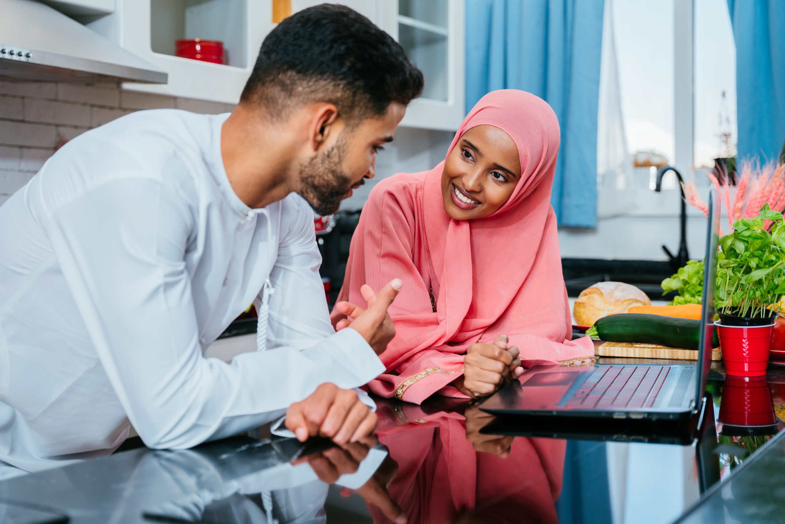 Happy middle-eastern couple wearing traditional arab clothing at home - Married arabian husband and wife bonding together in the apartment, concepts about relationship, domestic life and emirati lifestyle