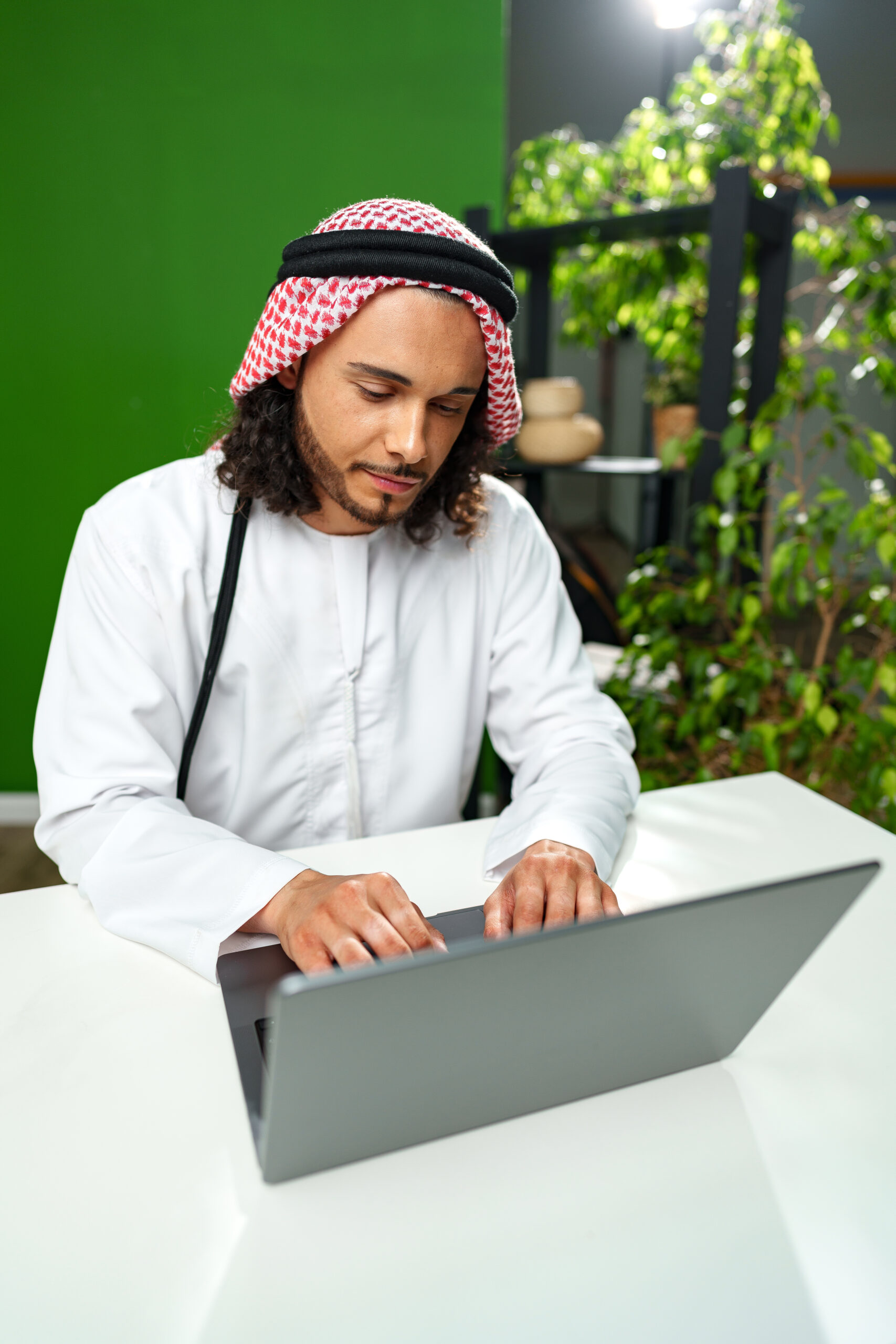 Young Arab man in traditional dress thobe working on computer in office close up